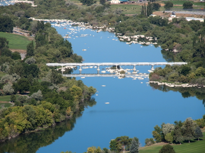 [A silver non-arched bridge spans the blue waters of the Snake River. Trees line both sides of the river and large white rocks protrude above the water's surface.]